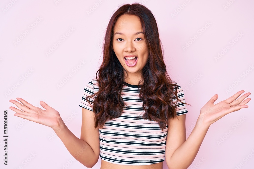 Young beautiful chinese girl wearing casual clothes celebrating victory with happy smile and winner expression with raised hands Young beautiful chinese girl wearing casual clothes celebrating victory with happy smile and winner expression with raised hands