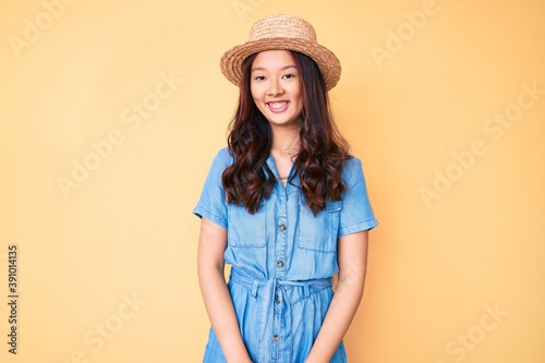 Young beautiful chinese girl wearing summer hat with a happy and cool smile on face. lucky person.