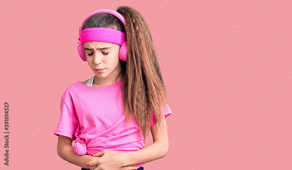 Cute hispanic child girl wearing gym clothes and using headphones with hand on stomach because indigestion, painful illness feeling unwell. ache concept. Cute hispanic child girl wearing gym clothes and using headphones with hand on stomach because indigestion, painful illness feeling unwell. ache concept.