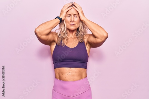 Middle age caucasian blonde woman wearing sportswear over pink background suffering from headache desperate and stressed because pain and migraine. hands on head. © Krakenimages.com