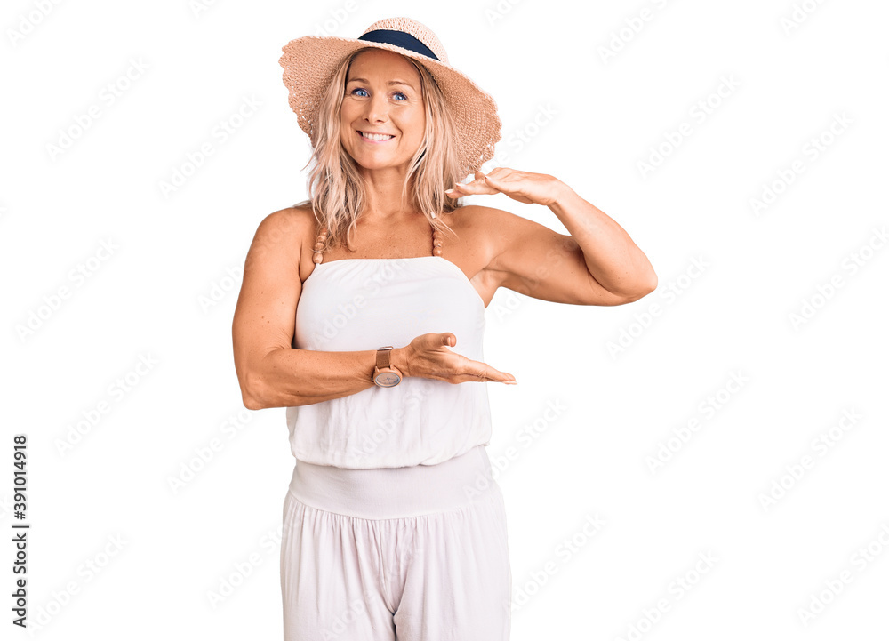 Middle age fit blonde woman wearing summer hat gesturing with hands showing big and large size sign, measure symbol. smiling looking at the camera. measuring concept. Middle age fit blonde woman wearing summer hat gesturing with hands showing big and large size sign, measure symbol. smiling looking at the camera. measuring concept.
