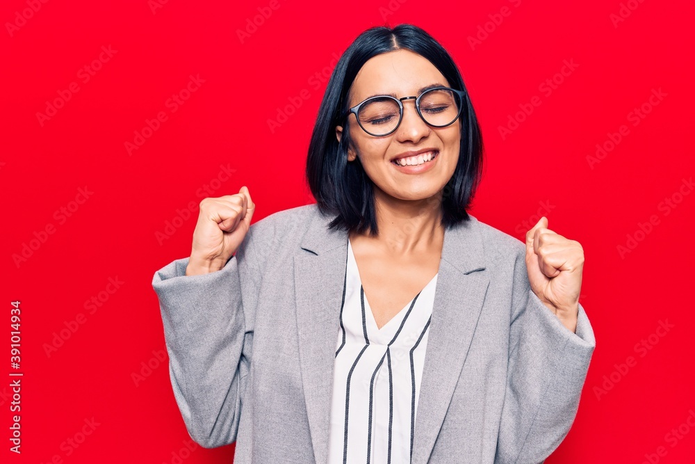 Young beautiful latin woman wearing business clothes celebrating surprised and amazed for success with arms raised and eyes closed Young beautiful latin woman wearing business clothes celebrating surprised and amazed for success with arms raised and eyes closed