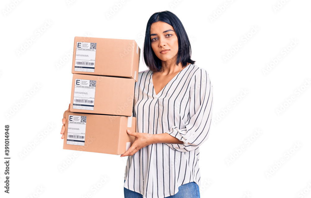 Young beautiful latin woman holding delivery package thinking attitude and sober expression looking self confident Young beautiful latin woman holding delivery package thinking attitude and sober expression looking self confident