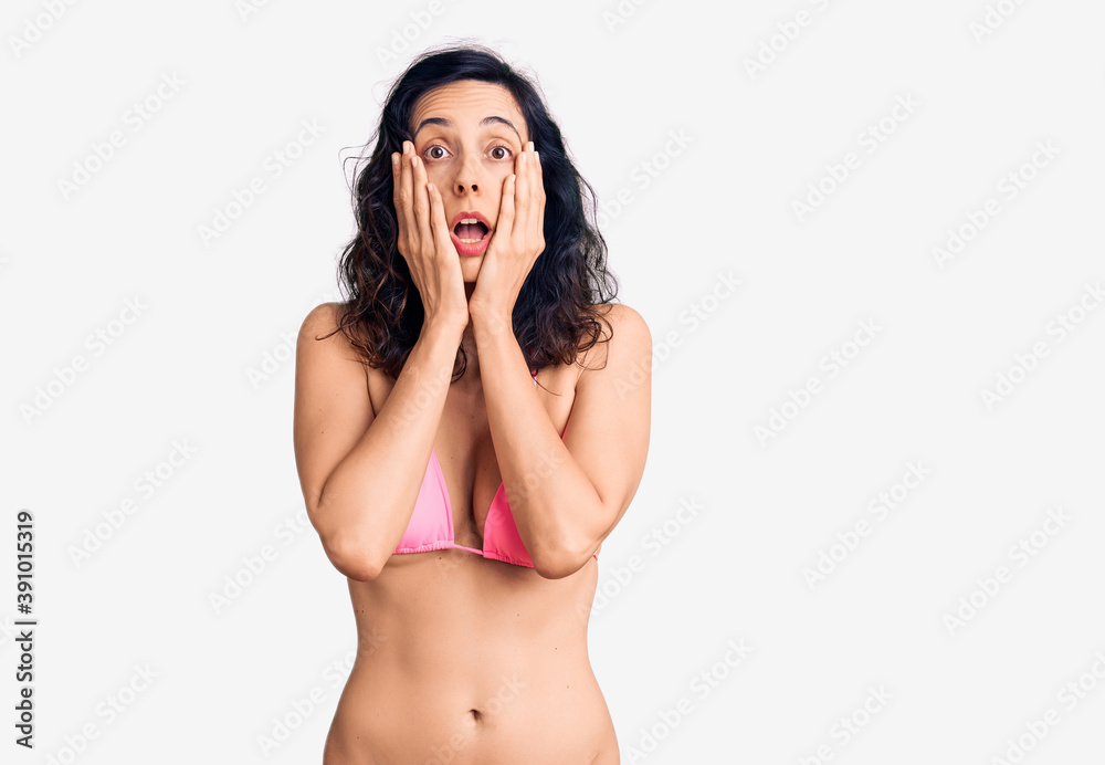 Young beautiful hispanic woman wearing bikini afraid and shocked, surprise and amazed expression with hands on face Young beautiful hispanic woman wearing bikini afraid and shocked, surprise and amazed expression with hands on face
