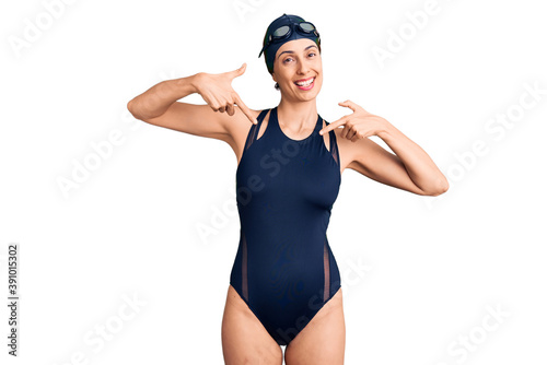 Young beautiful hispanic woman wearing swimwear and swimmer glasses looking confident with smile on face, pointing oneself with fingers proud and happy. © Krakenimages.com