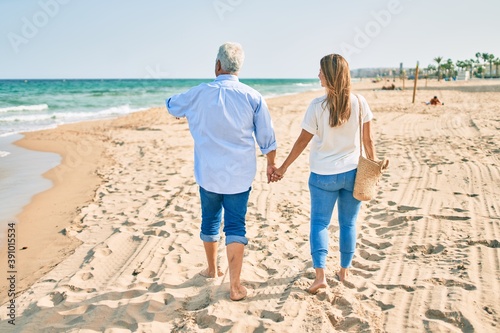 Middle age hispanic couple walking at the beach on back view.