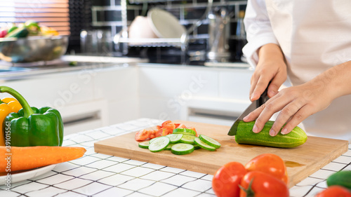 young Asian woman is preparing healthy food vegetable salad by Cutting cucumber for ingredients on cutting board on light kitchen  Cooking At Home and healthy food concept.