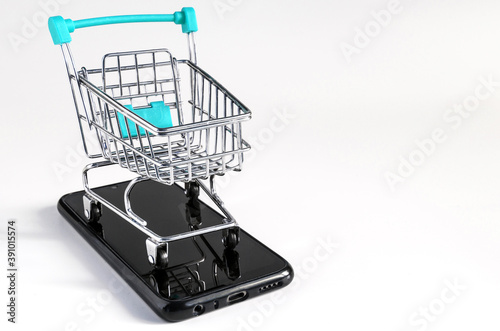 blue trolley at the supermarket, standing on the smartphone on a light background, the concept of online trading © Лозовая Людмила