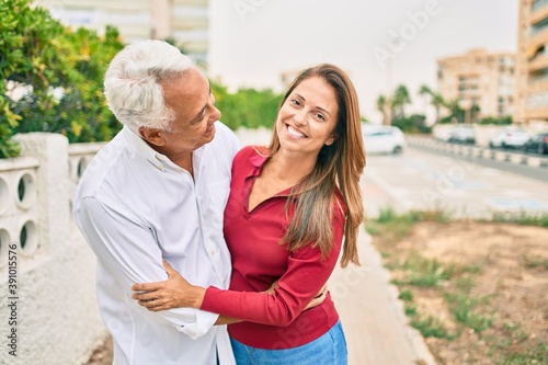 Middle age hispanic couple smiling happy and hugging walking at street.