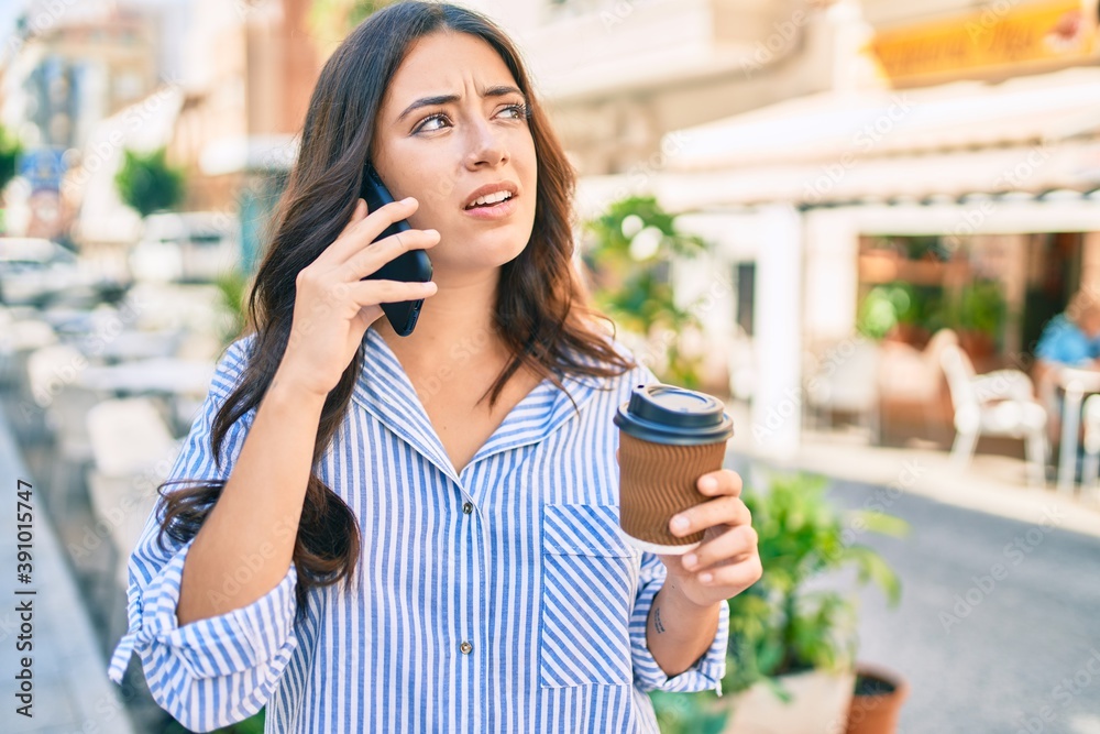 Young hispanic businesswoman talking on the smartphone and drinking take away coffee at the city.