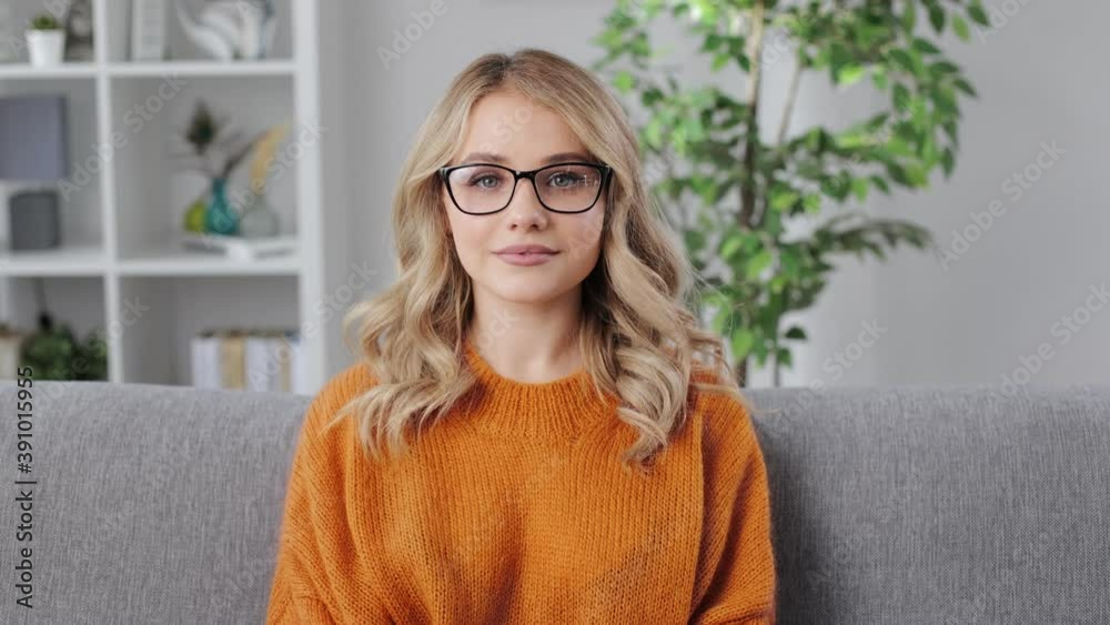 Portrait of young pretty lady with blond hair dressed in yellow sweater. Beautiful woman in eyeglasses sitting on cozy sofa at home. Portrait of young pretty lady with blond hair dressed in yellow sweater. Beautiful woman in eyeglasses sitting on cozy sofa at home.