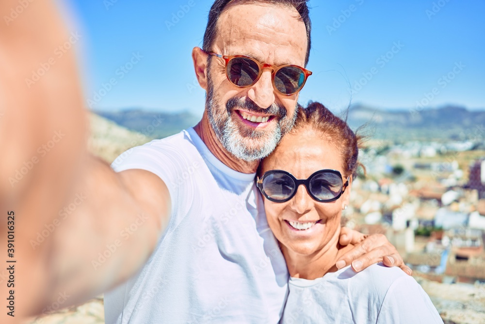 Middle age beautiful couple wearing casual clothes and sunglasses smiling happy. Standing with smile on face making selfie by the camera hugging at town street. Middle age beautiful couple wearing casual clothes and sunglasses smiling happy. Standing with smile on face making selfie by the camera hugging at town street.