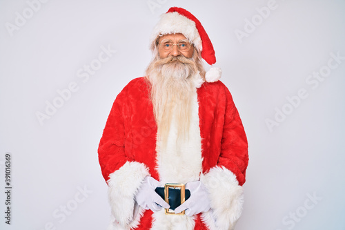 Old senior man with grey hair and long beard wearing santa claus costume with suspenders with a happy and cool smile on face. lucky person.