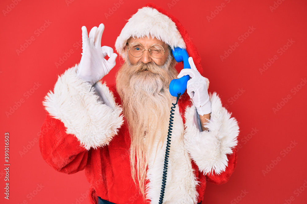 Old senior man wearing santa claus costume using vintage telephone doing ok sign with fingers, smiling friendly gesturing excellent symbol Old senior man wearing santa claus costume using vintage telephone doing ok sign with fingers, smiling friendly gesturing excellent symbol