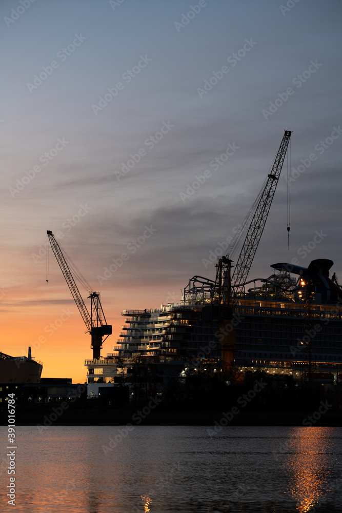 Silhouette of a cruise ship and tower cranes in a ship yard against sunrise