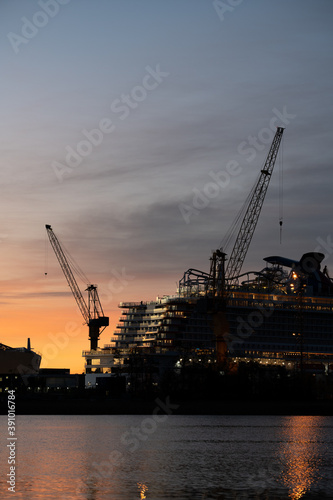 Silhouette of a cruise ship and tower cranes in a ship yard against sunrise