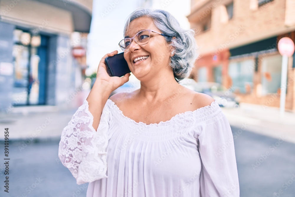 Middle age woman with grey hair smiling happy outdoors speaking on the phone