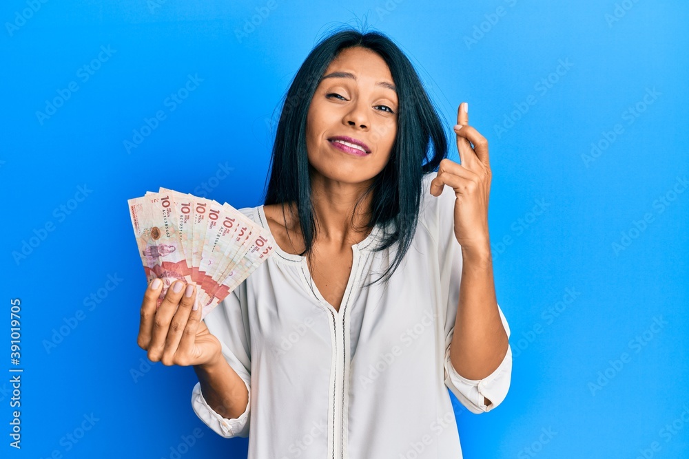 Obraz premium Young african american woman holding 10 colombian pesos banknotes gesturing finger crossed smiling with hope and eyes closed. luck and superstitious concept.