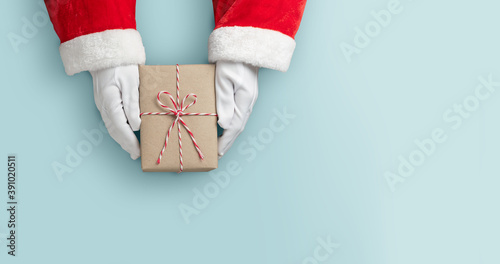 Top view of Santa claus hands is holding a brown gift box or present box over blue isolated background.