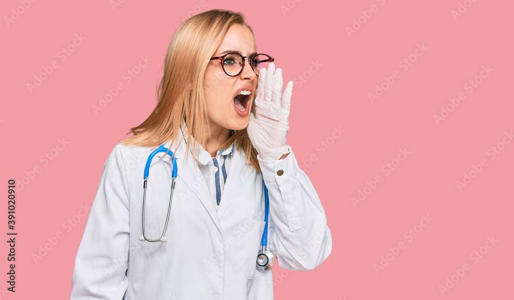 Beautiful caucasian woman wearing doctor uniform and stethoscope shouting and screaming loud to side with hand on mouth. communication concept. Beautiful caucasian woman wearing doctor uniform and stethoscope shouting and screaming loud to side with hand on mouth. communication concept.