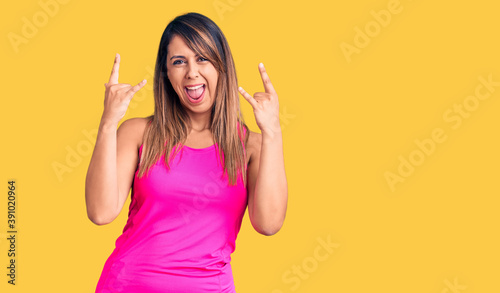 Young beautiful woman wearing sportswear shouting with crazy expression doing rock symbol with hands up. music star. heavy concept.