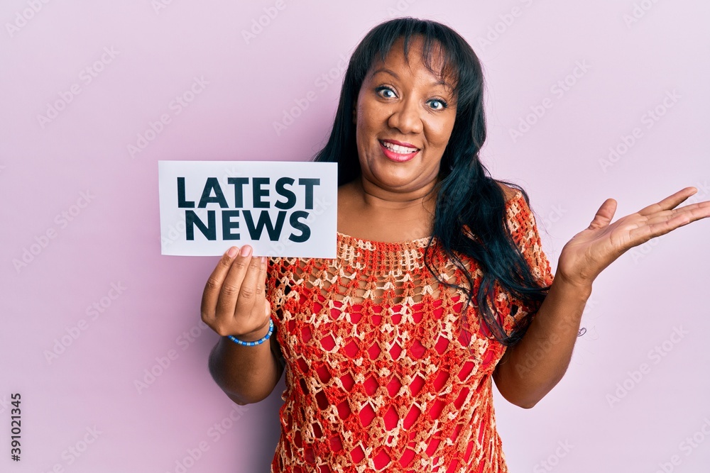 Middle age african american woman holding latest news message on paper celebrating achievement with happy smile and winner expression with raised hand