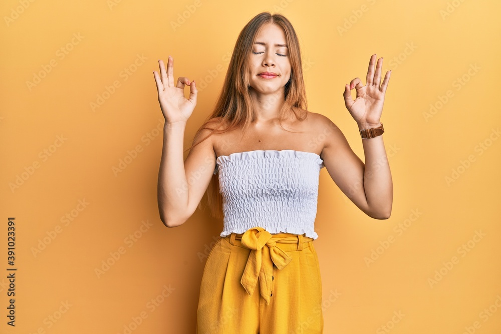 Beautiful young blonde woman wearing casual summer clothes relax and smiling with eyes closed doing meditation gesture with fingers. yoga concept. Beautiful young blonde woman wearing casual summer clothes relax and smiling with eyes closed doing meditation gesture with fingers. yoga concept.