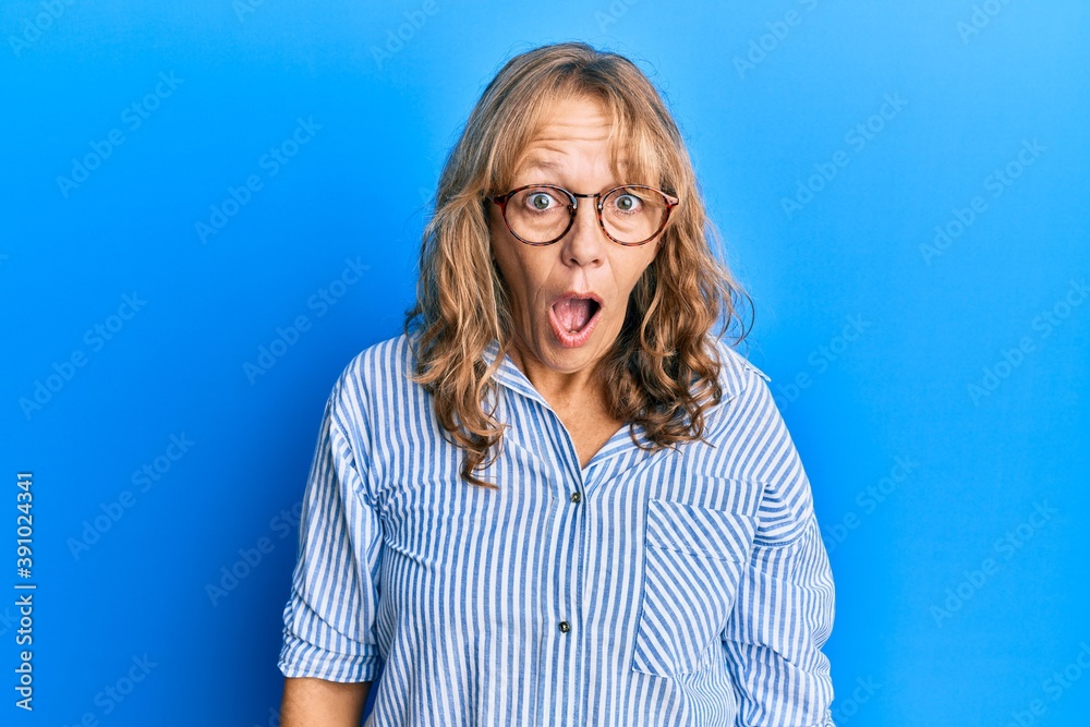 Middle age blonde woman wearing casual clothes and glasses afraid and shocked with surprise and amazed expression, fear and excited face.