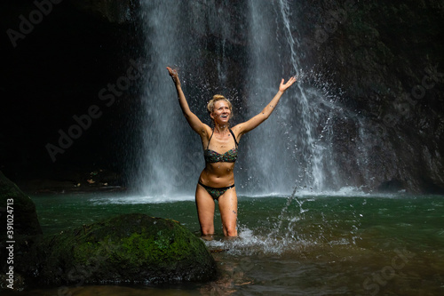 Young Caucasian woman with blond hair standing near the waterfall. Travel lifestyle. Leke Leke waterfall, Bali. photo