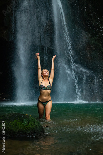Young Caucasian woman with blond hair standing near the waterfall. Travel lifestyle. Leke Leke waterfall  Bali.
