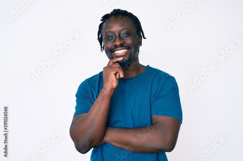 Young african american man with braids wearing casual clothes looking confident at the camera with smile with crossed arms and hand raised on chin. thinking positive.