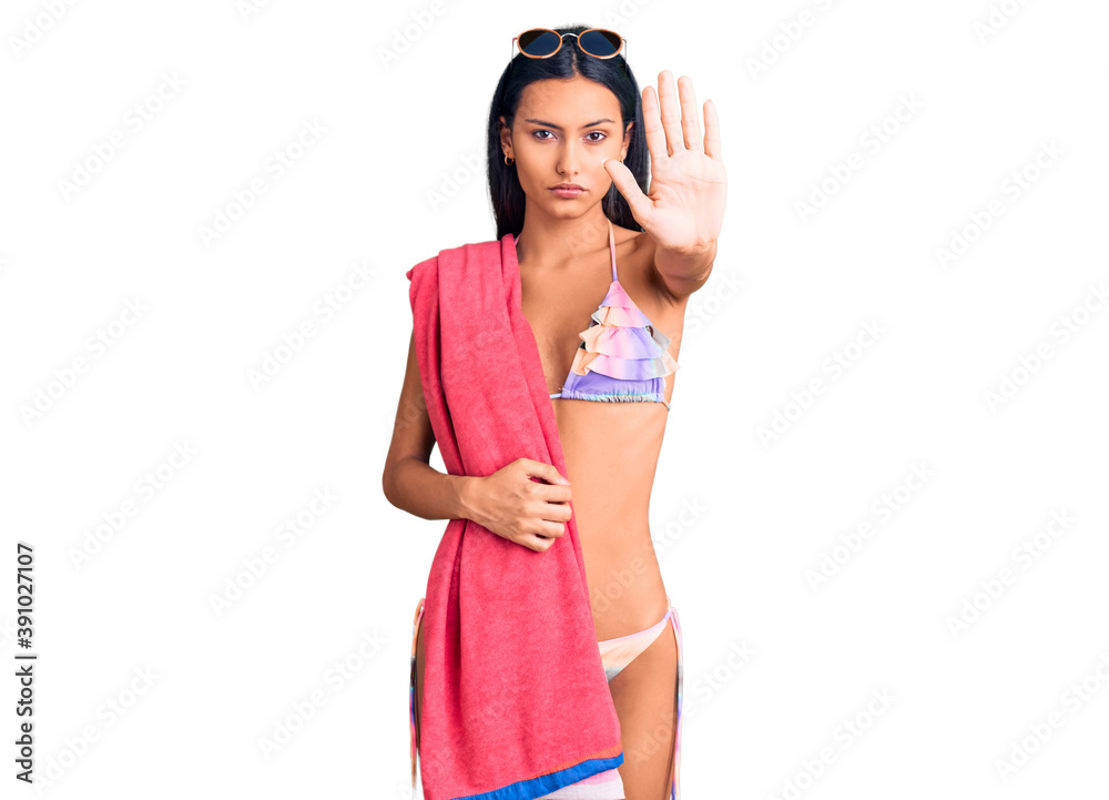Young beautiful latin girl wearing bikini and sunglasses with open hand doing stop sign with serious and confident expression, defense gesture