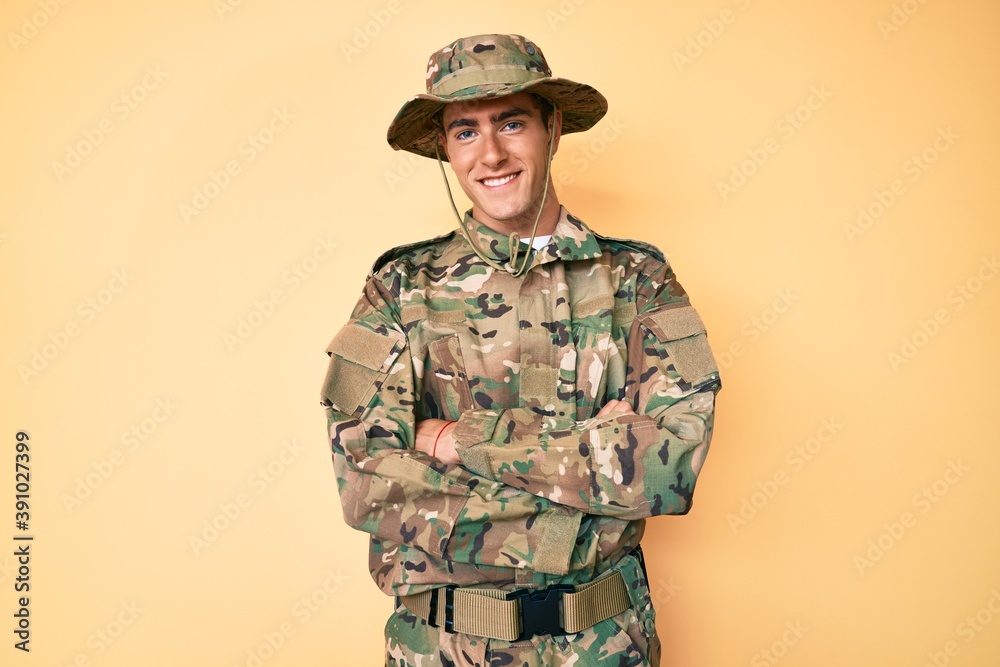 Young handsome man wearing camouflage army uniform happy face smiling with crossed arms looking at the camera. positive person. Young handsome man wearing camouflage army uniform happy face smiling with crossed arms looking at the camera. positive person.