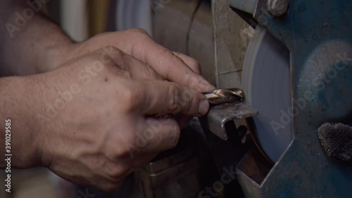 Locksmith sharpens a drill on emery in the workshop