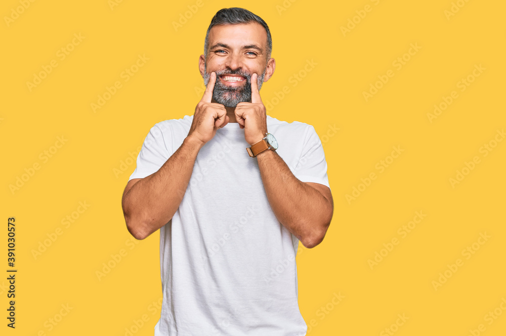 Middle age handsome man wearing casual white tshirt smiling with open mouth, fingers pointing and forcing cheerful smile Middle age handsome man wearing casual white tshirt smiling with open mouth, fingers pointing and forcing cheerful smile