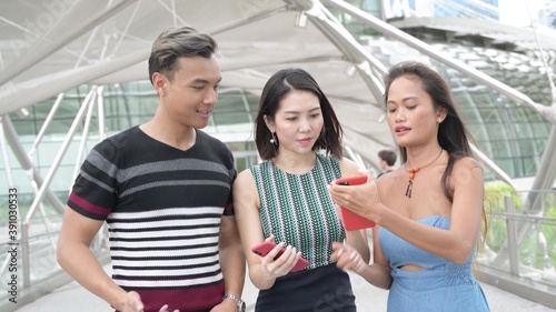 Three asian friends strolling in the city looking at the smartphone. Happiness and tourism concept