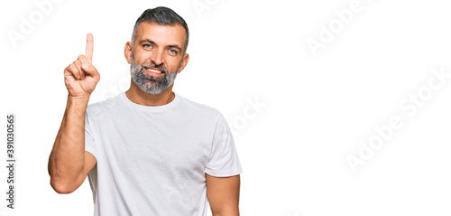 Middle age handsome man wearing casual white tshirt pointing finger up with successful idea. exited and happy. number one.