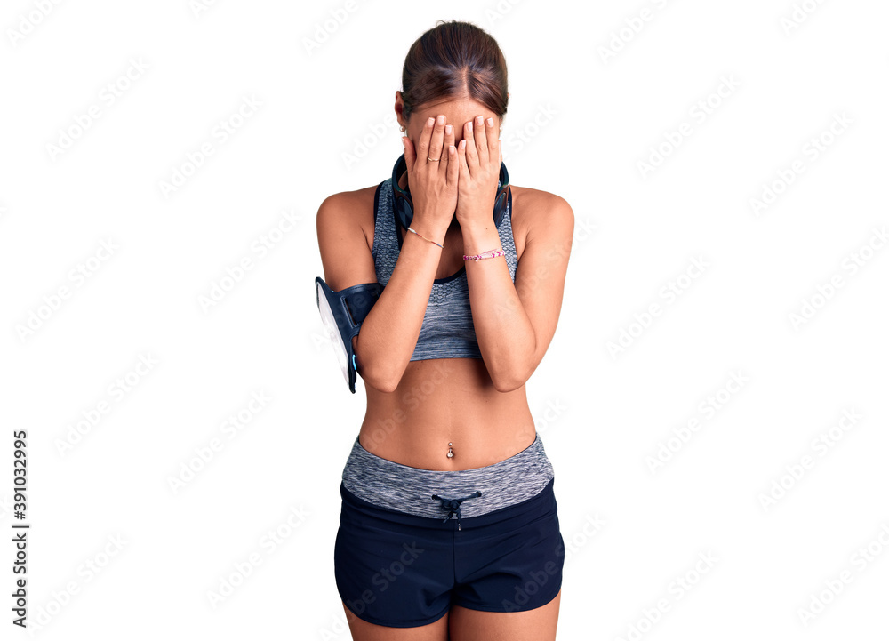 Young beautiful hispanic woman wearing gym clothes and using headphones with sad expression covering face with hands while crying. depression concept. Young beautiful hispanic woman wearing gym clothes and using headphones with sad expression covering face with hands while crying. depression concept.