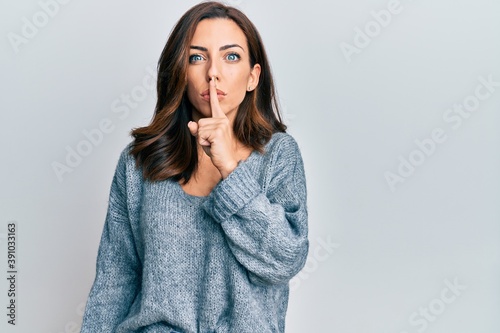 Young brunette woman wearing casual winter sweater asking to be quiet with finger on lips. silence and secret concept.