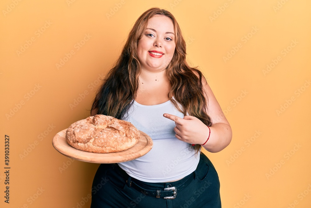 Plus size caucasian young woman holding bread smiling happy pointing with hand and finger Plus size caucasian young woman holding bread smiling happy pointing with hand and finger
