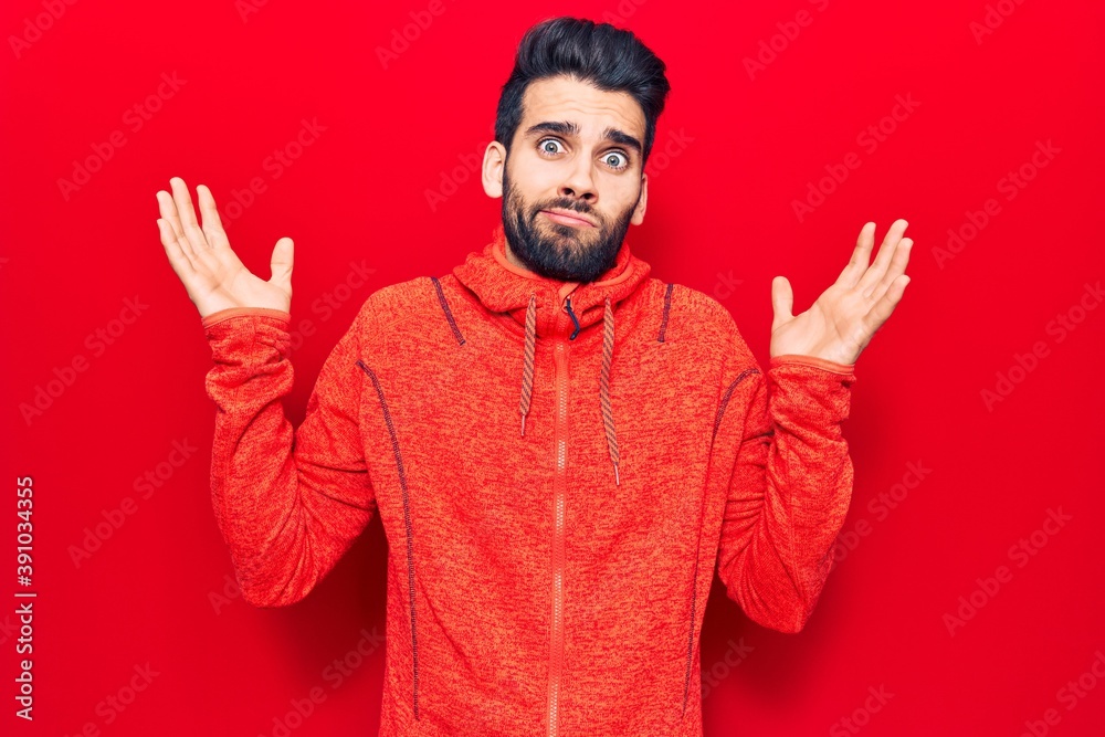 Young handsome man with beard wearing casual sweatshirt clueless and confused with open arms, no idea and doubtful face. Young handsome man with beard wearing casual sweatshirt clueless and confused with open arms, no idea and doubtful face.
