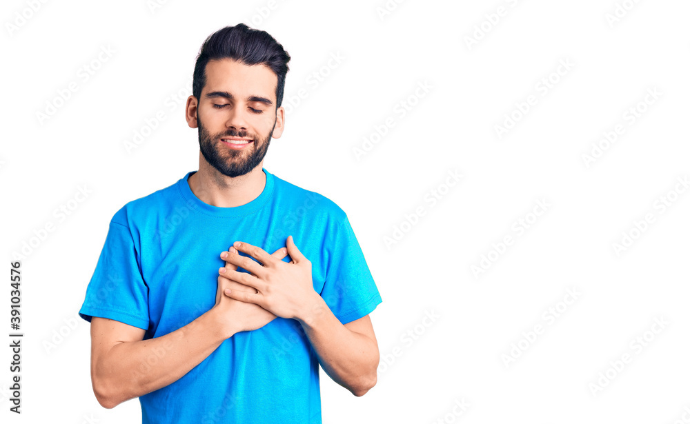 Young handsome man with beard wearing casual t-shirt smiling with hands on chest with closed eyes and grateful gesture on face. health concept. Young handsome man with beard wearing casual t-shirt smiling with hands on chest with closed eyes and grateful gesture on face. health concept.