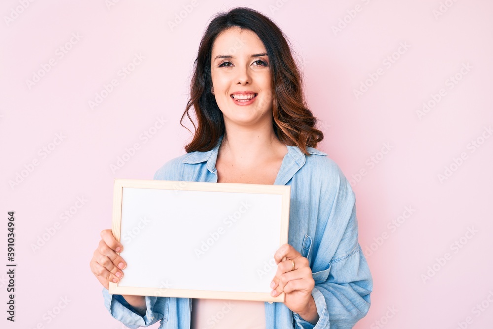 Young beautiful brunette woman holding blank empty banner looking positive and happy standing and smiling with a confident smile showing teeth Young beautiful brunette woman holding blank empty banner looking positive and happy standing and smiling with a confident smile showing teeth