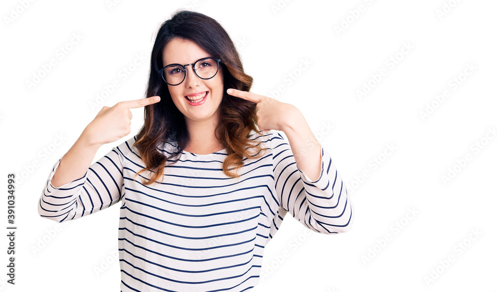 Beautiful young brunette woman wearing casual clothes and glasses smiling cheerful showing and pointing with fingers teeth and mouth. dental health concept. Beautiful young brunette woman wearing casual clothes and glasses smiling cheerful showing and pointing with fingers teeth and mouth. dental health concept.