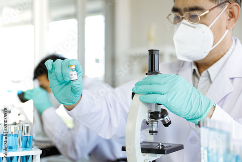 Healthcare professional in protective gloves & workwear holding & organising a tray of COVID-19 vaccine vials. The professional is carrying out researches on COVID-19 vaccine in laboratory.