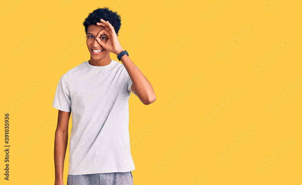 Young african american man wearing casual clothes doing ok gesture with hand smiling, eye looking through fingers with happy face. Young african american man wearing casual clothes doing ok gesture with hand smiling, eye looking through fingers with happy face.