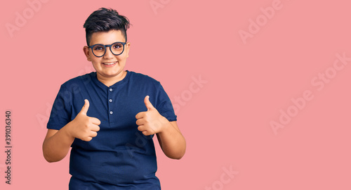 Fotografie Little boy kid wearing casual clothes and glasses success sign doing positive gesture with hand, thumbs up smiling and happy
