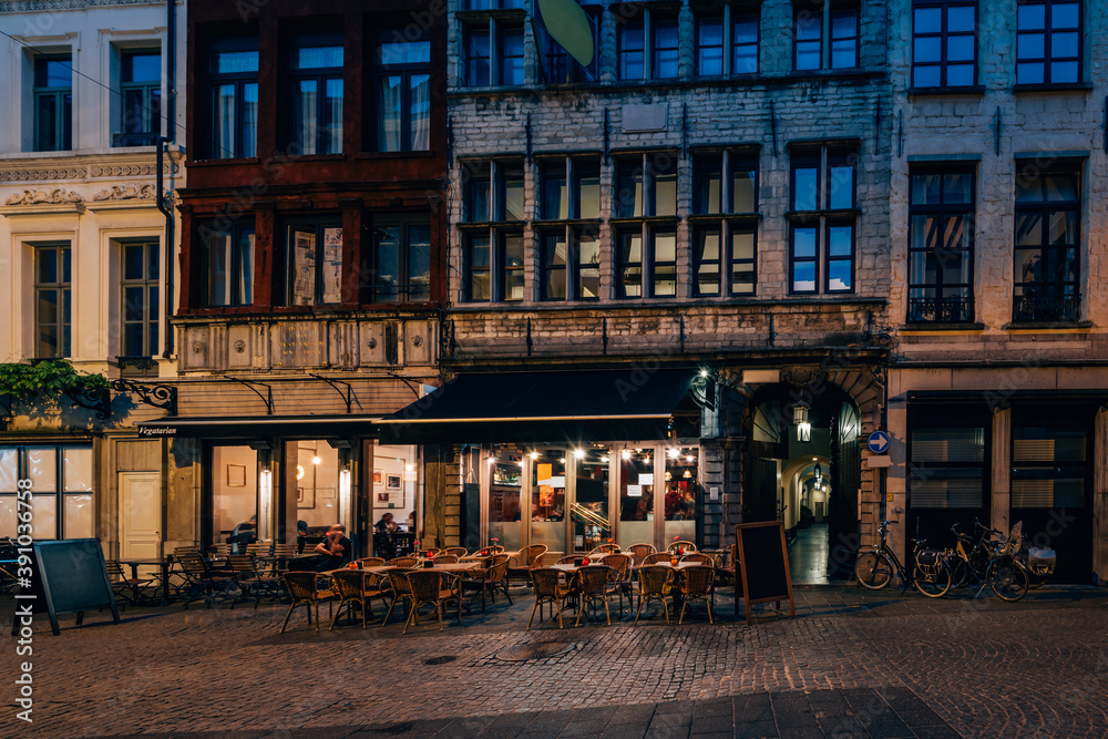 Old cozy narrow street with tables of restaurant in historic city center of Antwerpen (Antwerp), Belgium. Night cityscape of Antwerp. Architecture and landmark of Antwerpen