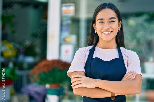 Young latin shopkeeper girl with arms crossed smiling happy standing at the florist photo