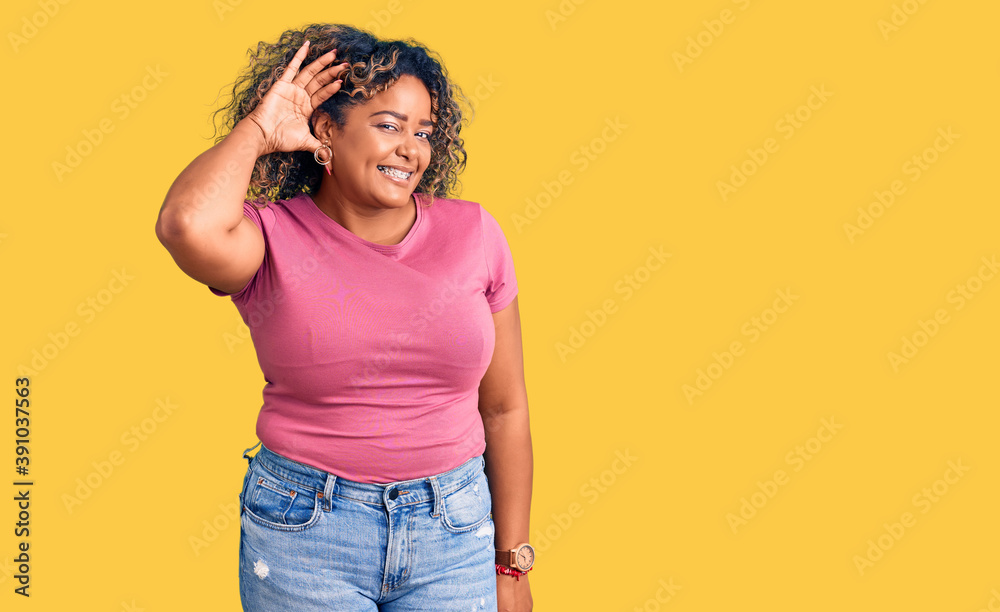 Young african american plus size woman wearing casual clothes smiling with hand over ear listening an hearing to rumor or gossip. deafness concept. Young african american plus size woman wearing casual clothes smiling with hand over ear listening an hearing to rumor or gossip. deafness concept.